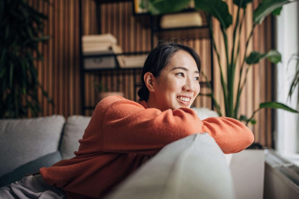 Smiling woman relaxing at home by the window on a cozy sofa